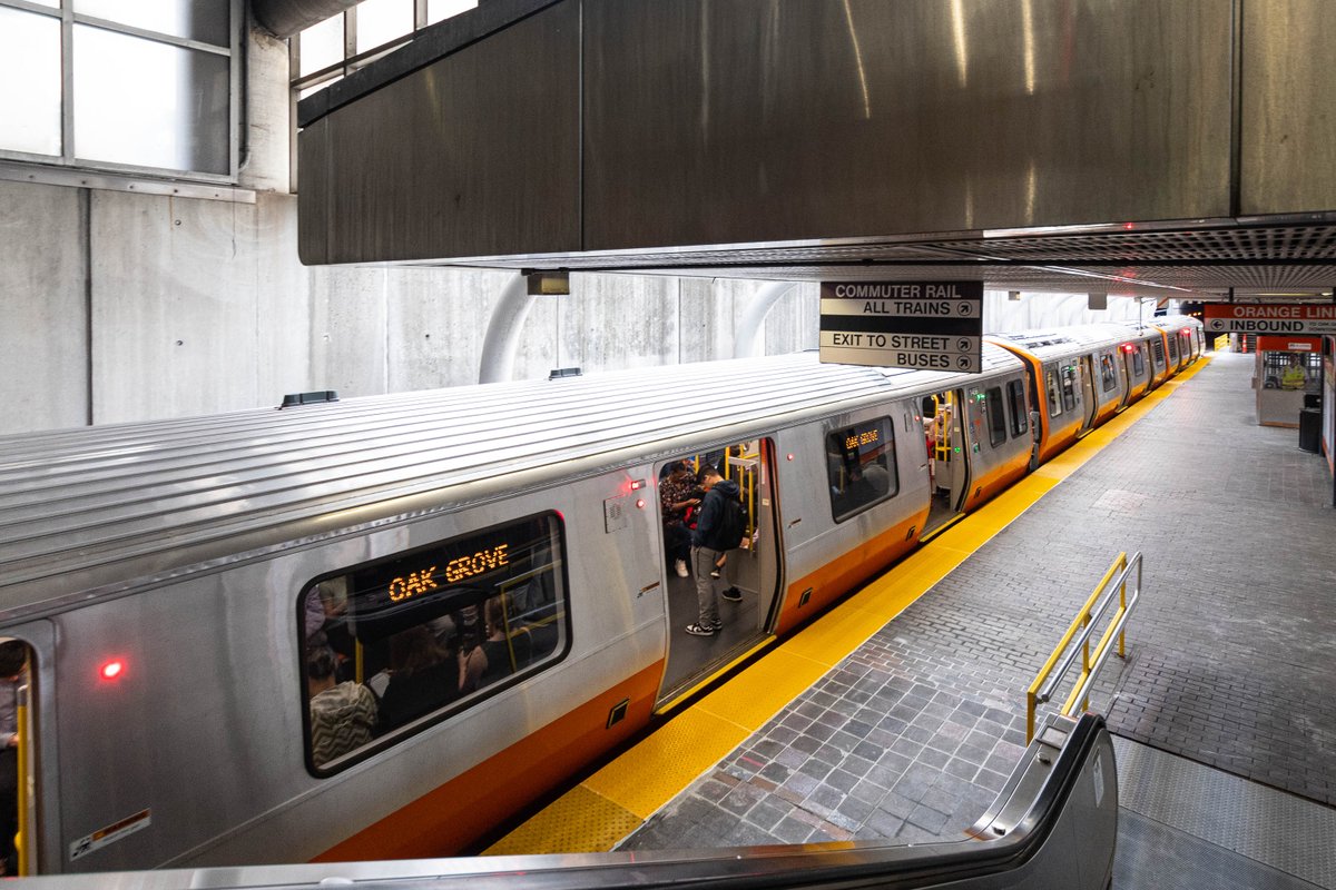 A new Orange Line train stopped at Ruggles station with its doors open, looking at the newly installed yellow tactile edges on the platform.