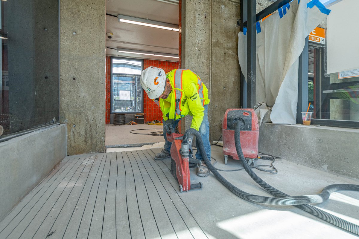 A construction worker in yellow safety vest and hard hat using a cutting tool to carve grooves into the new terrazzo flooring at Oak Grove station.