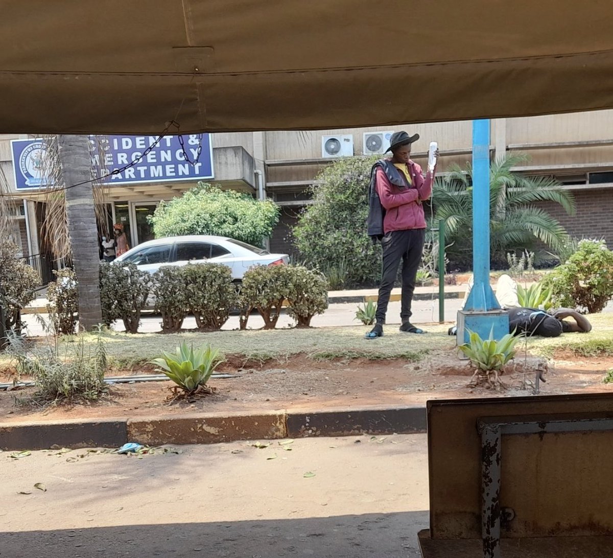 This happened today at Parirenyatwa Hospital.

A young man helping his friend by holding a drip pack outside the hospital.

This should be monitored by medical staff, but the system has broken down.

He is lying on the ground in the sun, that drip should be on a drip stand.

#Sad