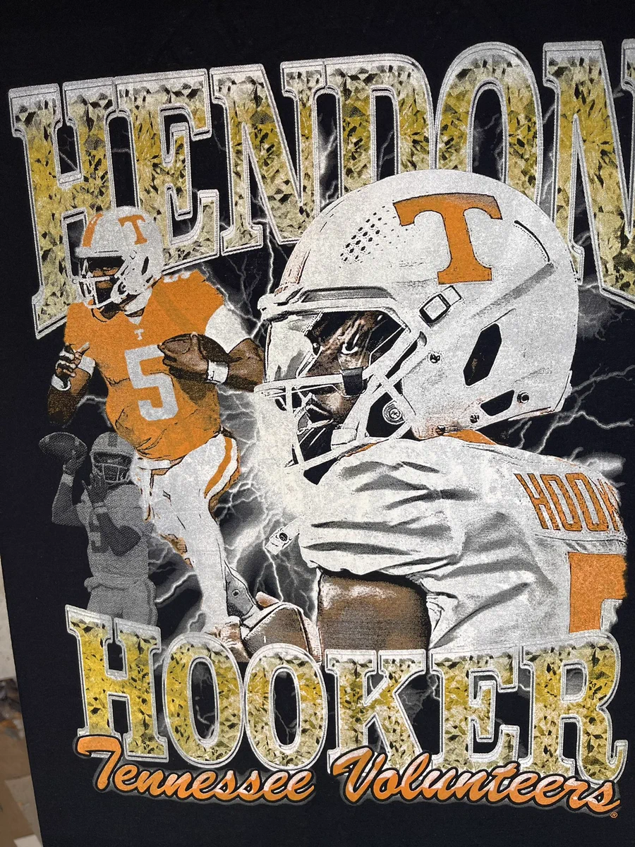 A close up of a Hendon Hooker NIL tee. It’s black with 3 photos of Hooker and his name in gold bling,