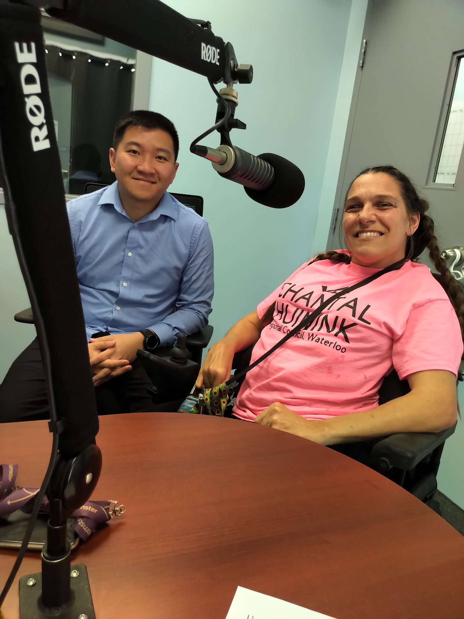 Chantal sits in front on a microphone on a large stand in a radio station recording room. The radio host sits beside her. 