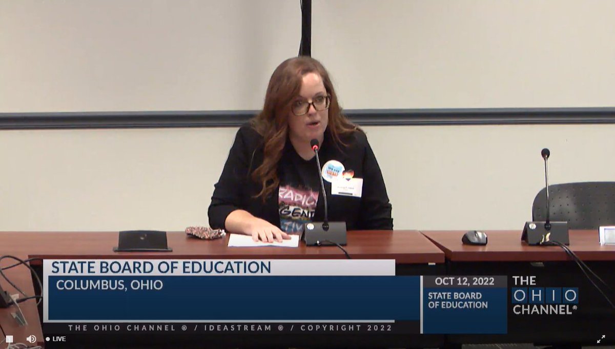 woman wearing trans flag colors speaking at a table