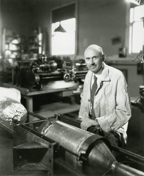 Robert Goddard in workshop sitting in front of rocket piece. 