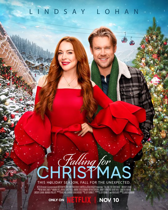 Lindsay Lohan is wearing a bold red jumpsuit with huge feathered sleeves and a bow at the waist. Chord Overstreet stands behind her in a flannel jacket with green scarf. Both are smiling while standing on front of a winter wonderland in the poster for their new move, Falling For Christmas. On Netflix November 10. 