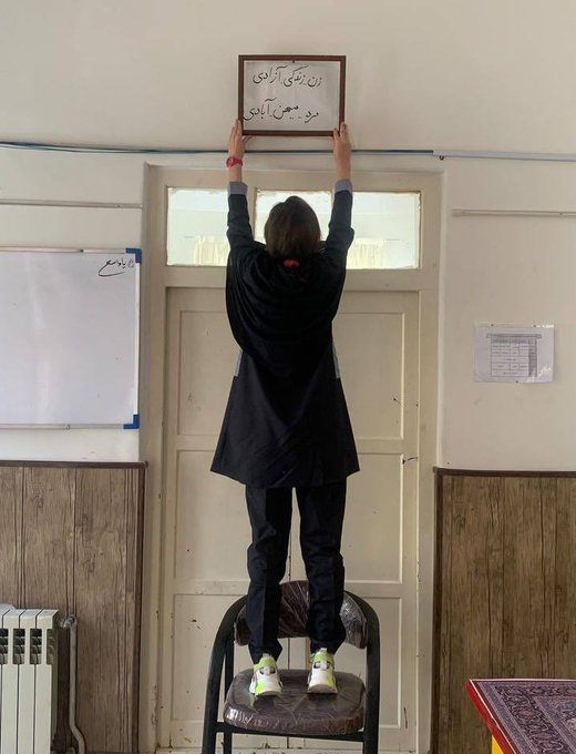 An Iranian schoolgirl without a head covering holds a "woman, life, freedom; man, homeland, rebuilding" sign in class