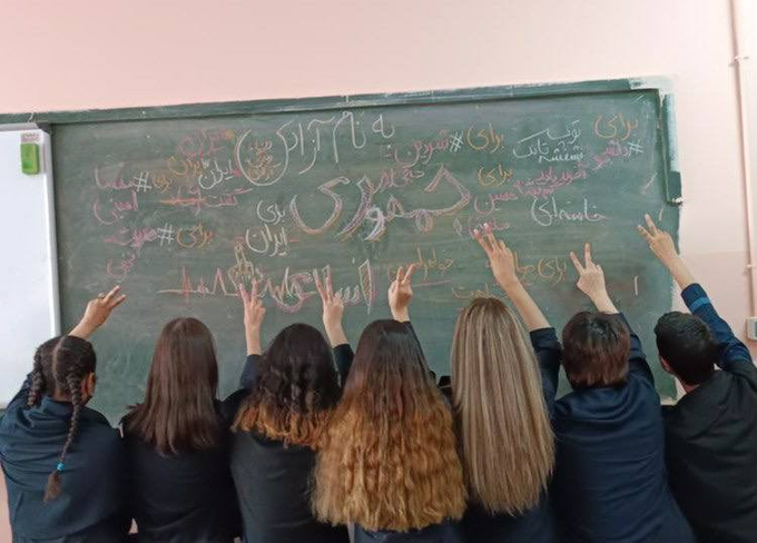 Iranian schoolgirls pose with victory signs in front of protest solgans and hashtags