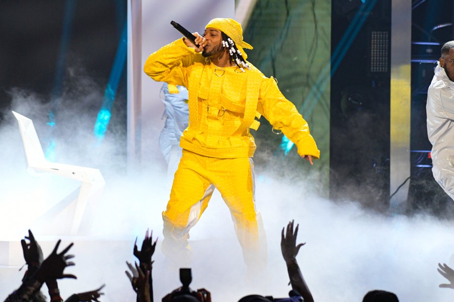 Armani is wearing a yellow jumpsuit and bandana 
