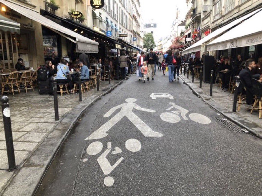 BrentToderian's tweet photo. Can streets really be transformed into people-places while still allowing cars? Not if you try to treat them equally. Cars need to be tamed — prioritized last — usually moving no faster than strollers walk. The relative size of images on this #Paris street conveys the priority. https://t.co/NaKVNSGPmH
