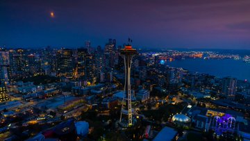 Aerial photo of the Space Needle and Seattle skyline at sunset with buildings lit up blue.