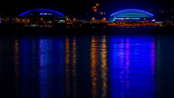 Photo of Lumen Field and T-Mobile Park lit up blue and reflecting off the water. 