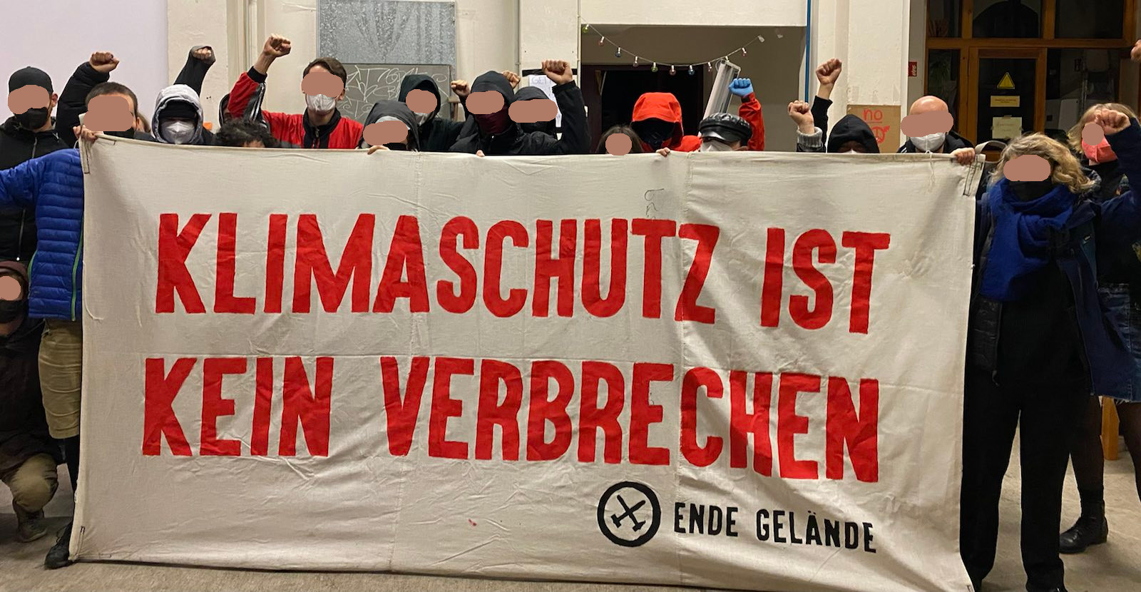 Banner mit der Aufschrift "Klimaschutz ist kein Verbrechen" dahinter einige Menschen mit in die Luft gestreckter Faust