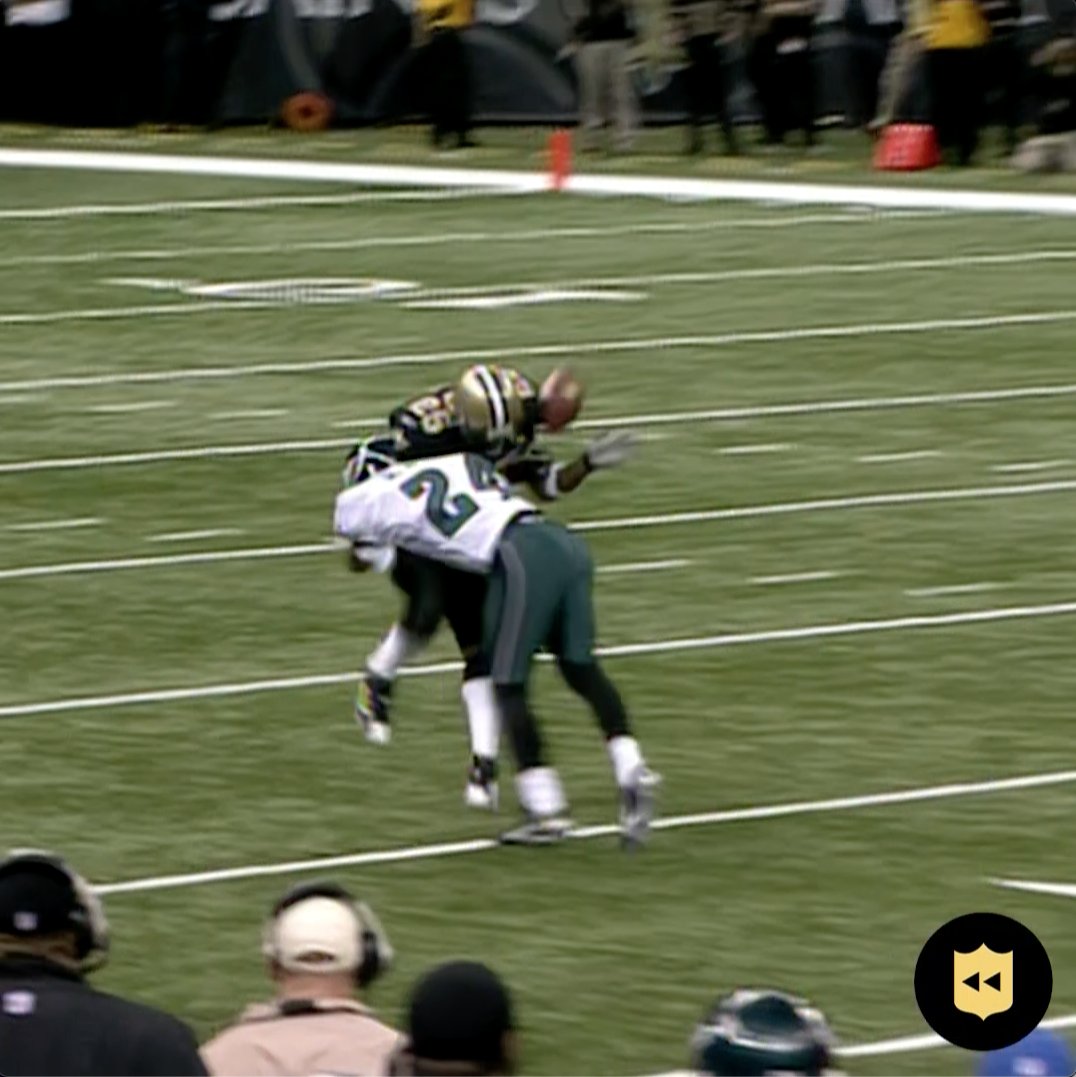 An American football game scene showing a player in a dark jersey tackling a player in a white and green jersey (number 25), with a football in mid-air above them on the field.