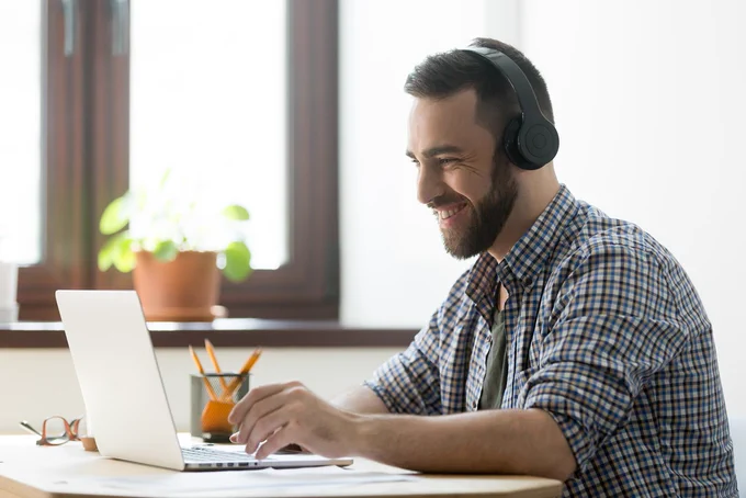 Man in checked shirt sitting at a desk looking at a laptop computer