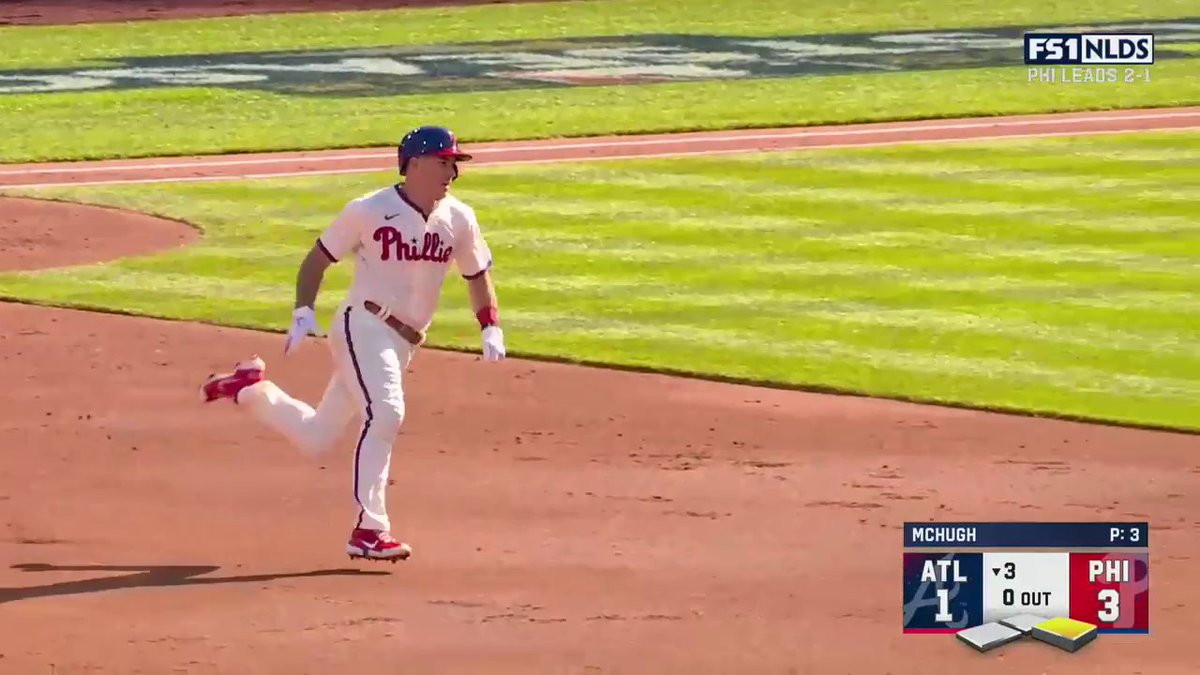A Philadelphia Phillies baseball player runs the bases in a white uniform, with the scoreboard showing ATL 1, PHI 3 in the bottom of the 3rd inning with 0 outs, and 'FS1 NLDS PHI LEADS 2-1' displayed.