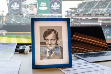 Photo of former Mariners broadcaster, Dave Niehaus, in the radio booth with T-Mobile Park in the background. 