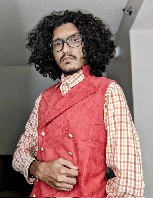 A photo of myself wearing a coral-colored corduroy vest on top of an orange gingham button up.