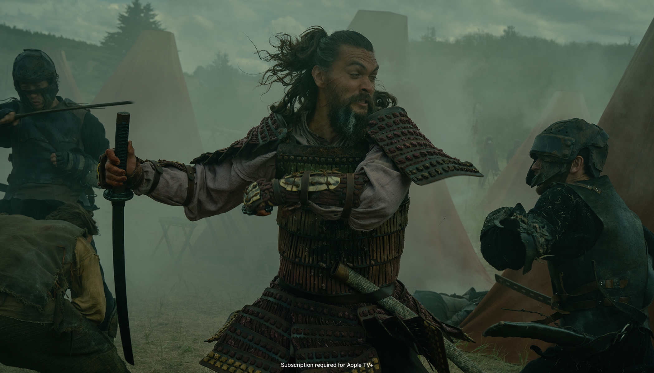 Jason Momoa as Baba Voss. He’s slinging a katana blade while dressed like a samurai. His target is a smaller man in armor who looks like he has no hope to survive the oversized Baba. Behind them in the fog, a battle unfolds in a green hue, as if the yellow hope of Season 1 and the blue despair of Season 2 are now mixed in a green of uncertainty.
