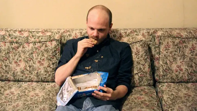 Man sitting on couch eating cookies.