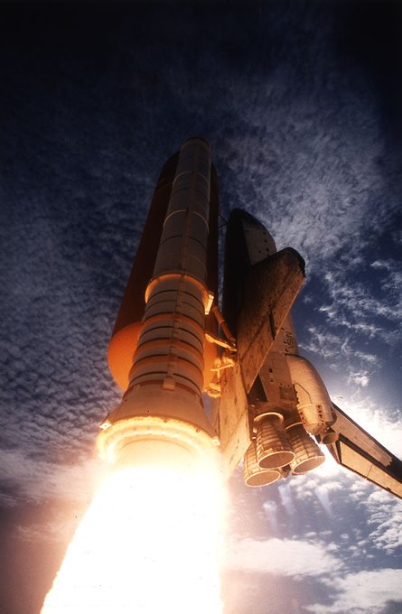 View from below of Space Shuttle Columbia lifting off with a blaze of firey exhaust into a deep blue sky on October 20, 1995.