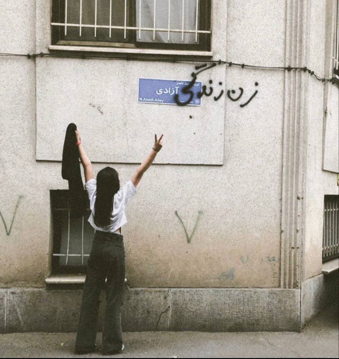 A young Iranian woman without a hijab sprays the words 'woman' and 'life' before a sign for 'azadi' [freedom] alleyway in Tehran to make the slogan 'woman, life, freedom'. 📸 via @Vahid #مهسا_امینی