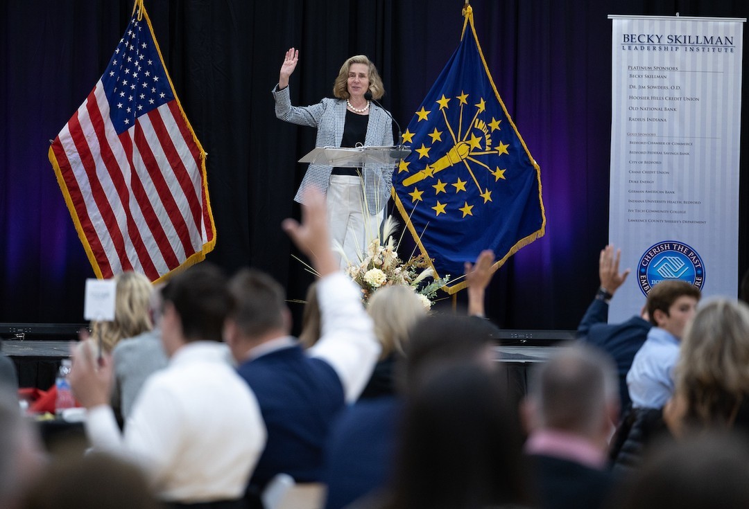 IU President Whitten speaks to a room of people in business attire on a podium in front of an Indiana flag at the Becky Skillman Leadership Institute in Bedford, IN.