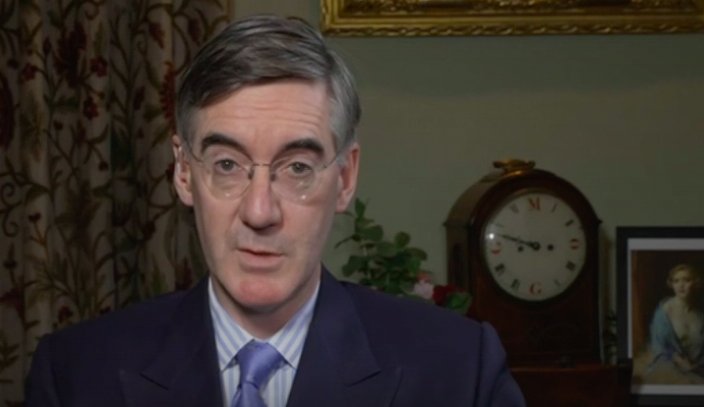 Jacob Rees Mogg conducts an interview in front of a clock which has Mogg written on it (2022)
