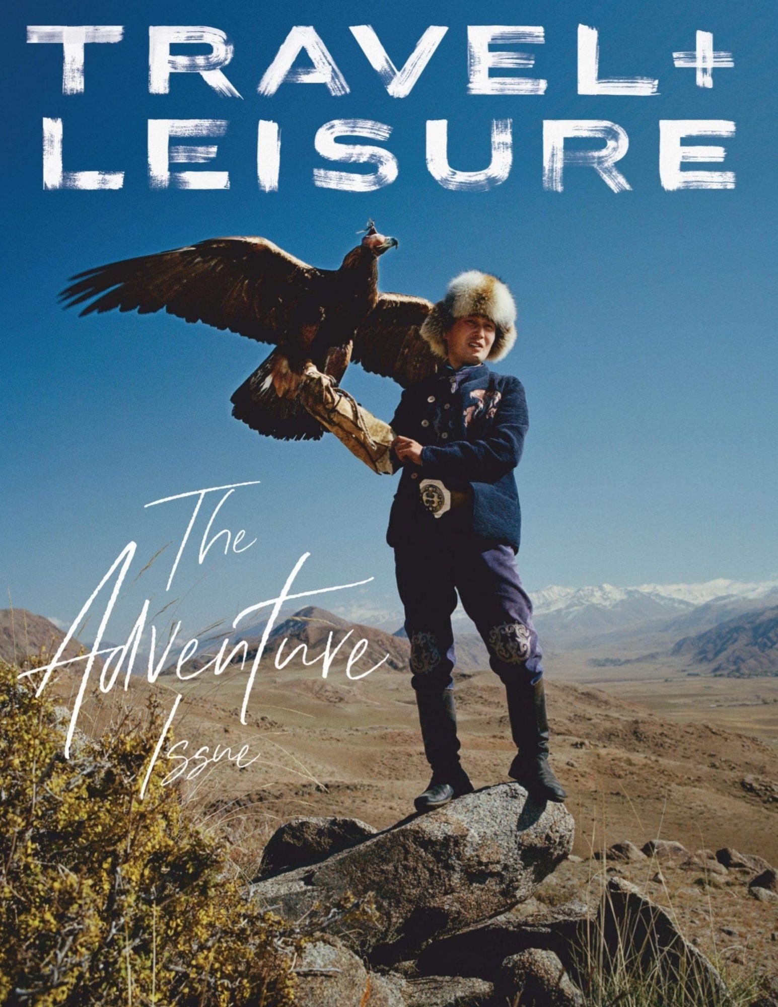 Cover of Travel + Leisure, Adventure Issue. A person with an eagle is standing in the middle of a huge valley