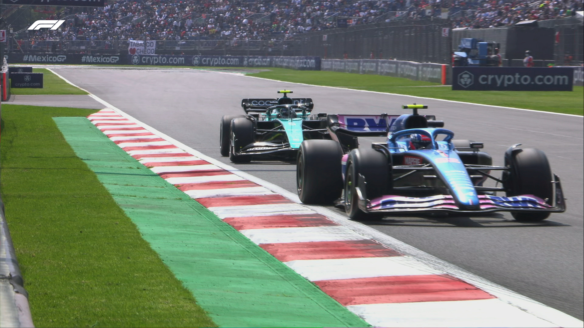 The Alpine of Jack Doohan is seen on track, braking for a corner. The Aston Martin of Sebastian Vettel can be seen behind him, as can a large crowd