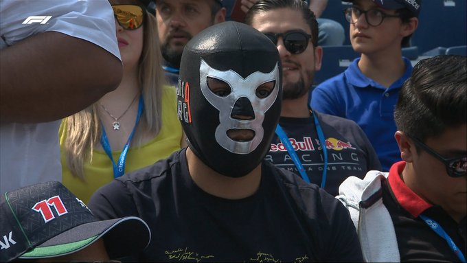 A fan in a bright silver and black traditional Mexican wrestler mask watches on from the crowd