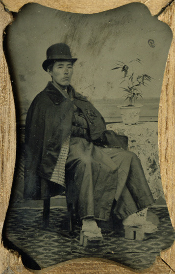 Ambrotype portrait, housed in a kiri-wood case, of a Japanese gentleman, identified on verso as “Kobayashi Shozaemon, 25 years old” wearing a yukata, coat, hat and geta. Photographed in 1882.