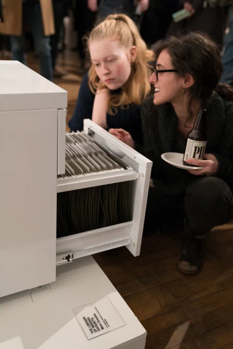 Photo by Mimi Ọnụọha of two people looking through a filing cabinet symbolic of data injustice, with espresso in hand.