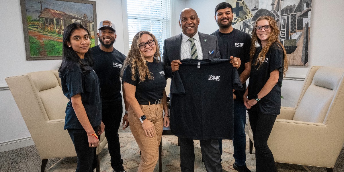 USCUpstate's tweet photo. Some of our talented Cybersecurity students stopped by Chancellor Harris' office to gift him one of their new "What is Your Digital Footprint" T-shirts, designed by Studio Upstate. We are so excited that soon we will graduate our first student from this tough program. Stay tuned! https://t.co/YhYtXnuEHV