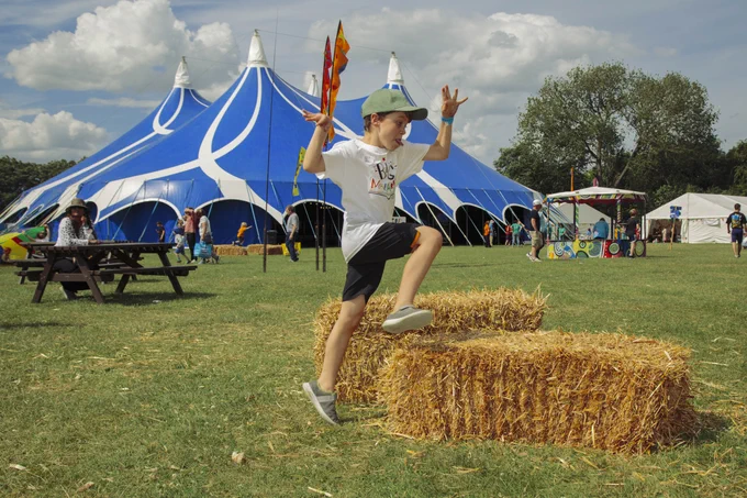 Boy climbing on hay bales in a field with a blue big top behind him