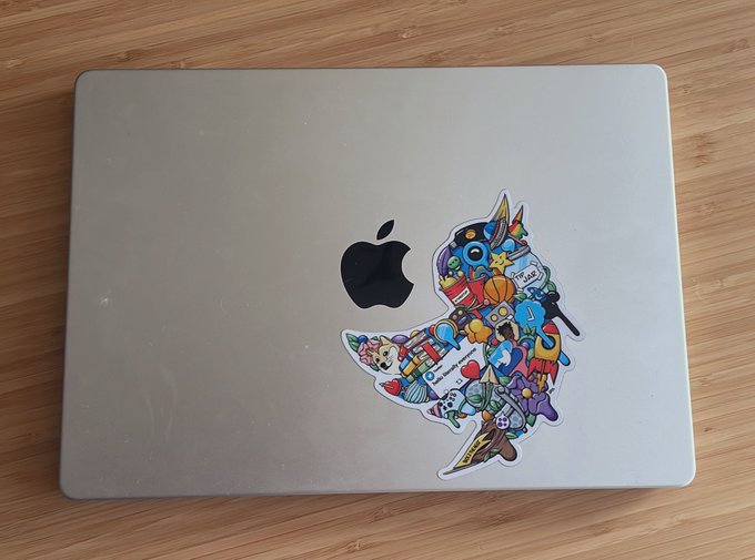 A closed MacBook Pro with a single multicolored and stylized Twitter sticker, resting on top of a desk.