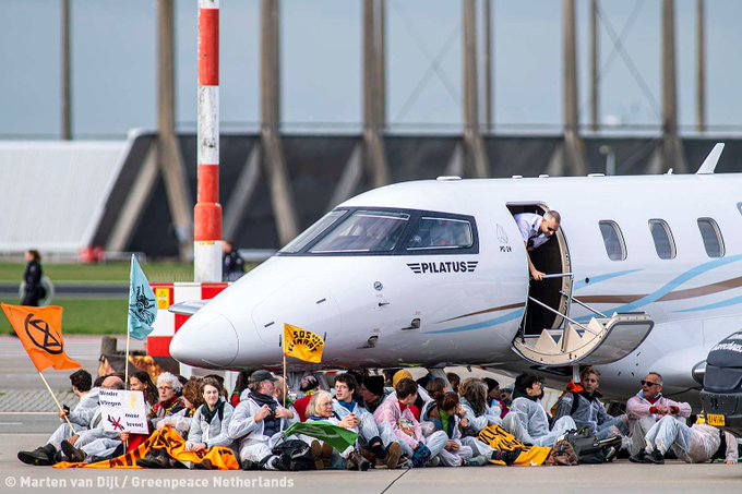 The front of a private jet is surrounded by sitting activists.