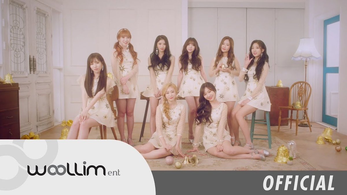 A promotional photo from Woollim Entertainment showing nine female K-pop idols posing together in matching white and gold star-patterned dresses in an elegantly decorated room.