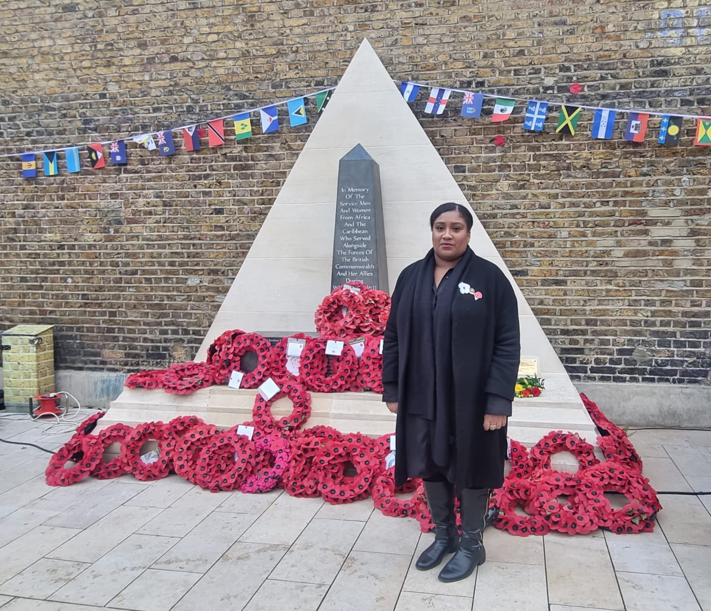 Bell standing at the Commonwealth Memorial in Windrush Square with dozens of wreaths laid and Commonwealth flag bunting running over it.