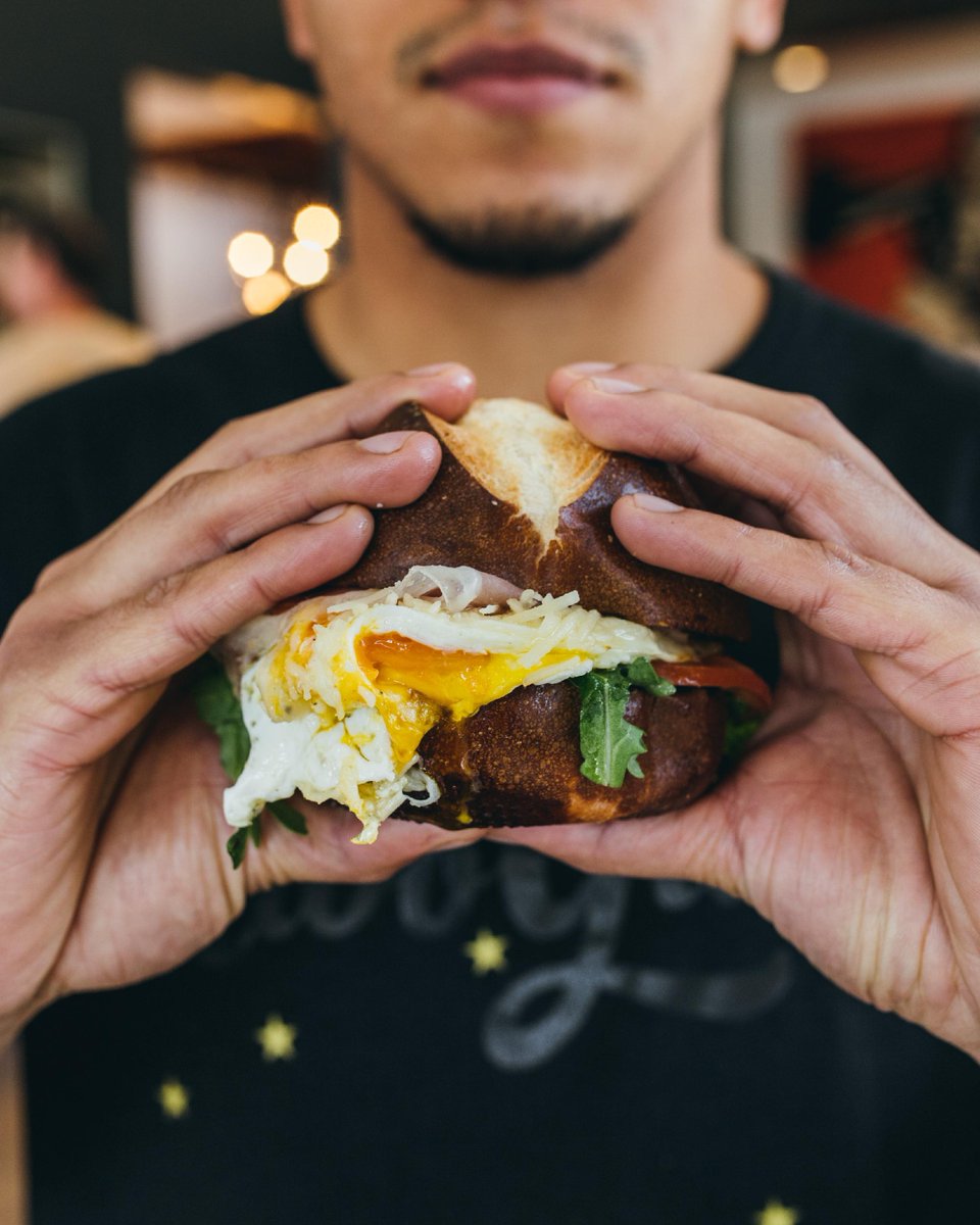 twogunsespresso's tweet image. Take me to wherever the Stanwich is served. 

#ImageDescriptions: A man holds the original Stanwich, a breakfast sandwich featuring fried egg, pesto, arugula, and tomato on a pretzel bun. The second image shows a green street sign indicating the street&apos;s name is Stanwich.

#Tw...