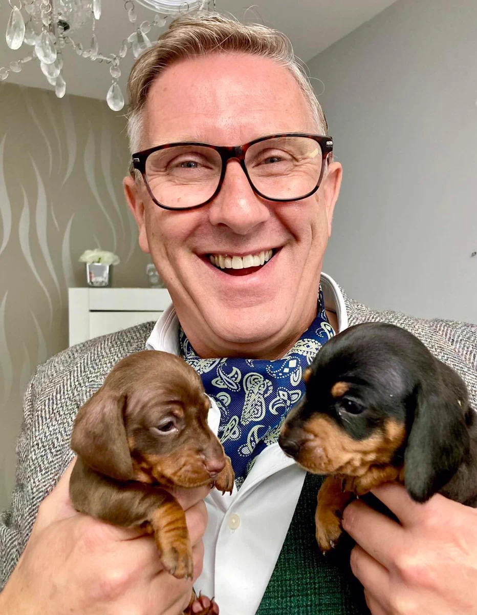 Graeme with a great big smile holding two dachshund puppies