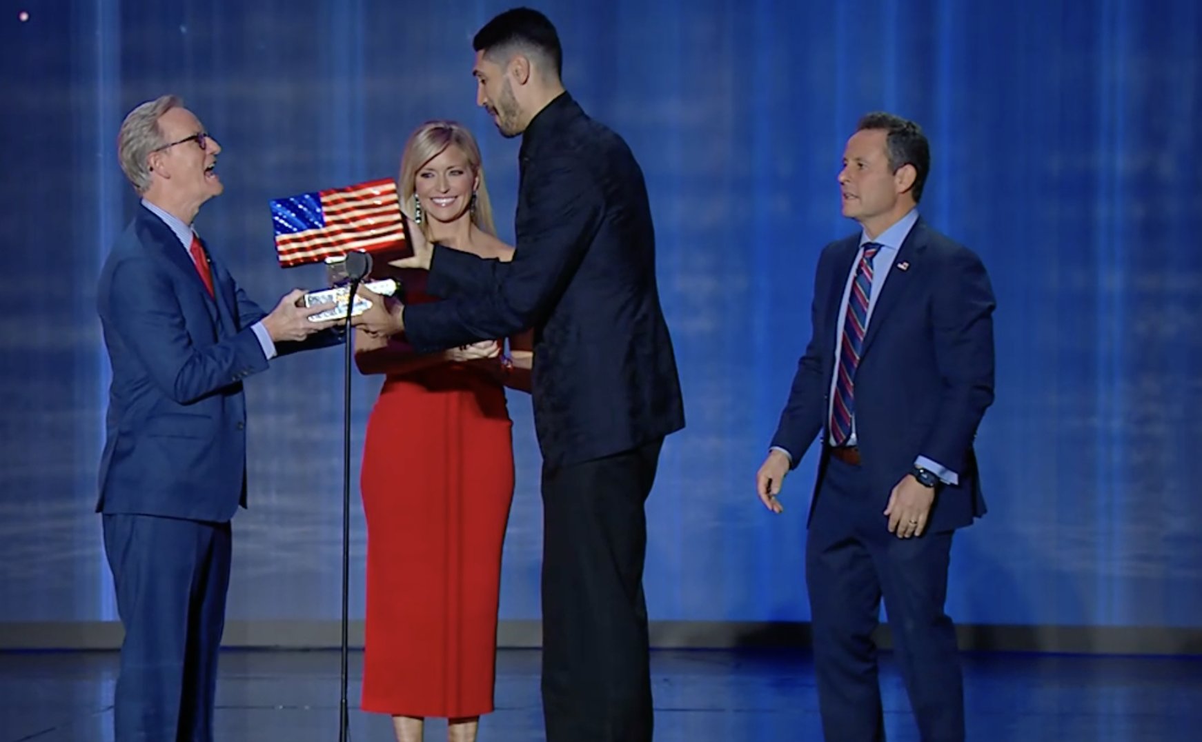 Enes Kanter Freedom accepts a large, heavy American flag trophy from Steve Doocy, Ainsley Earhardt, and Brian Kilmeade
