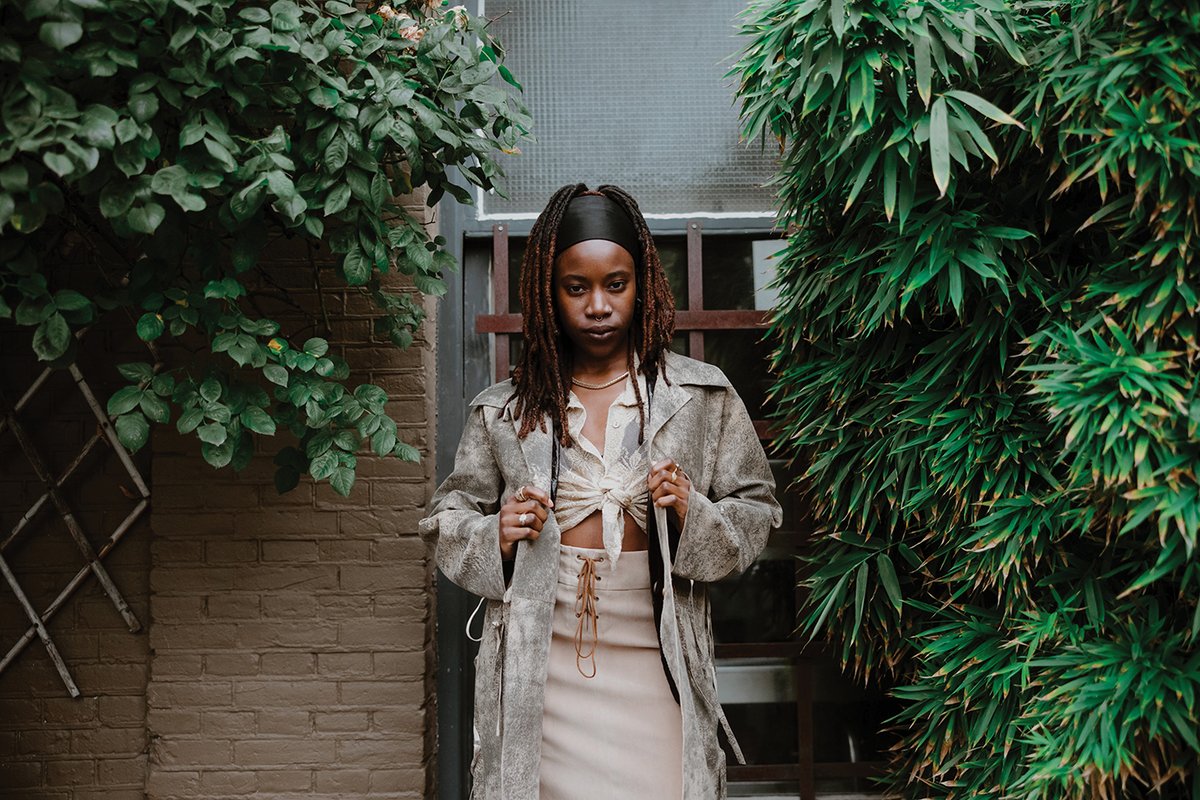 Gabrielle Kwarteng standing in front of a window next to two green hedges