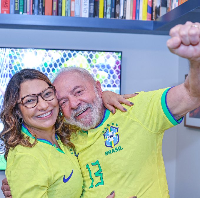 Janja e Lula se abraçam e comemoram jogo do Brasil. Lula veste camiseta amarela com número 13