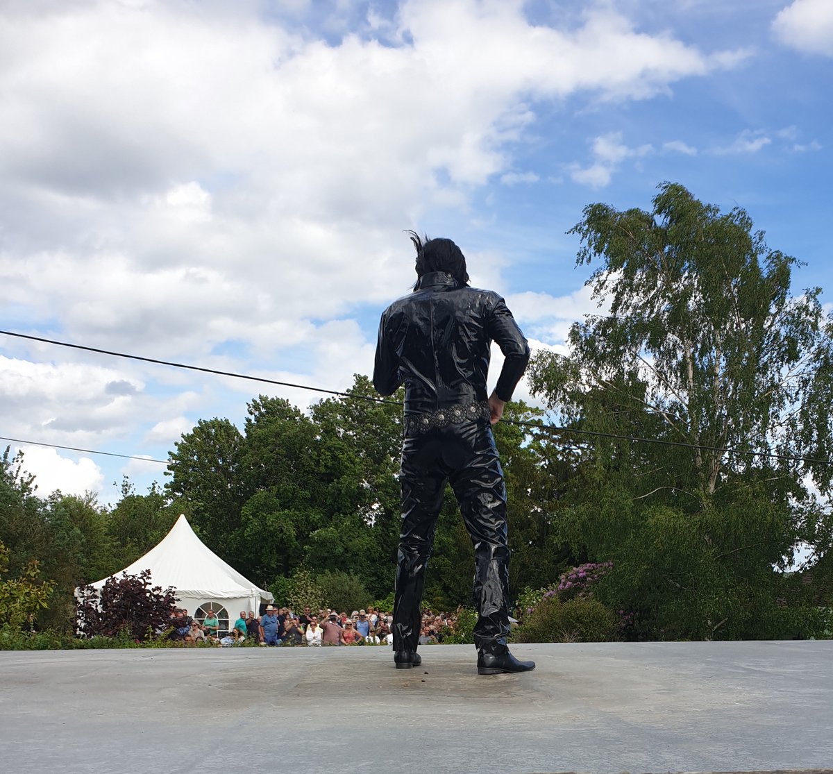 One of the first Plastic Elvis performances. Singing on a roof across a main road to stunned people in the pub garden opposite. The band are playing in the tent.