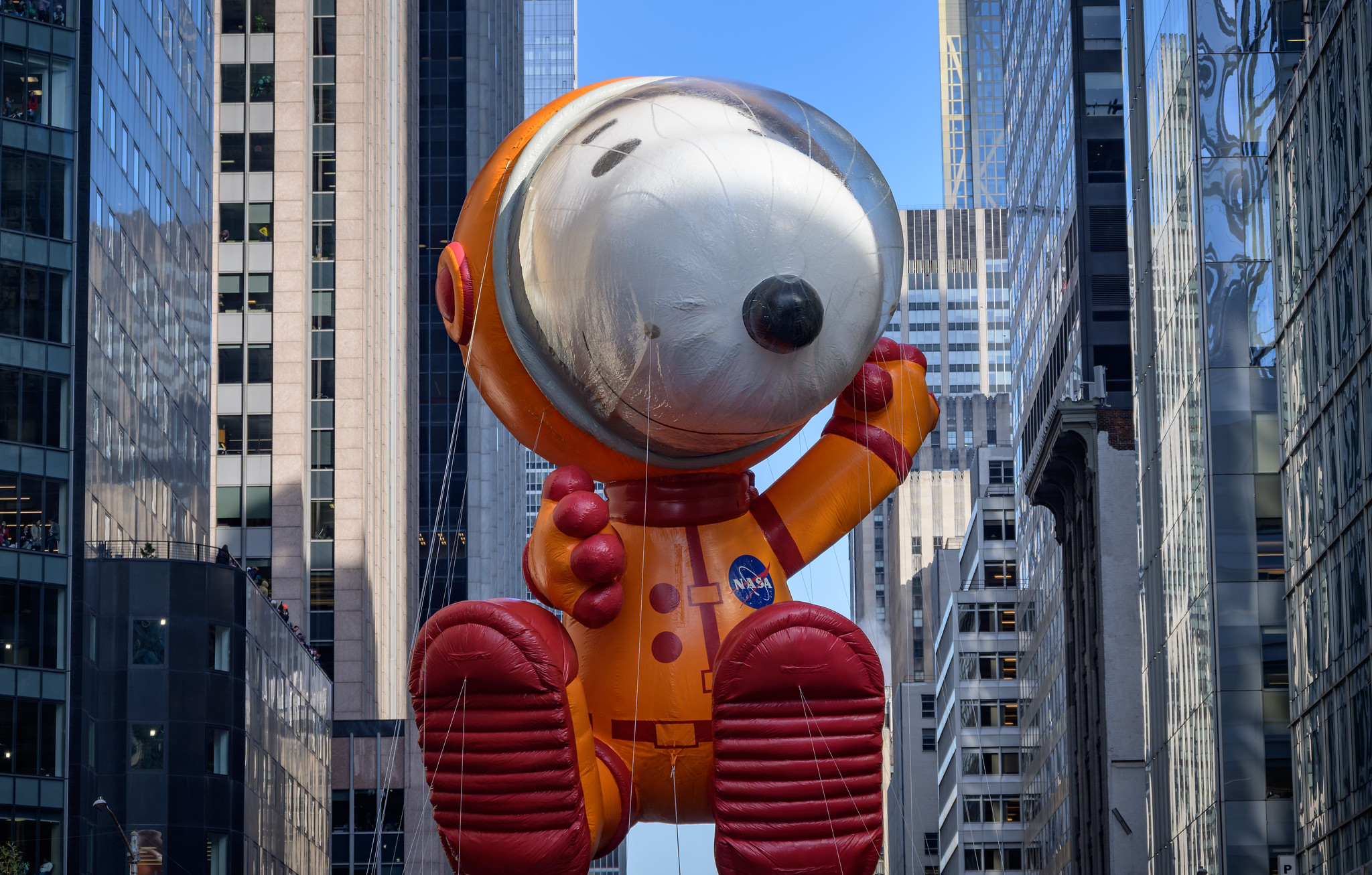 A large inflatable Snoopy float drifts down the streets of New York City in a parade. Snoopy, a caricature of a white dog with black eyes and a black snout, is dressed in the bright orange flight suit and visor helmet donned by NASA astronauts. Credit: NASA/Bill Ingalls