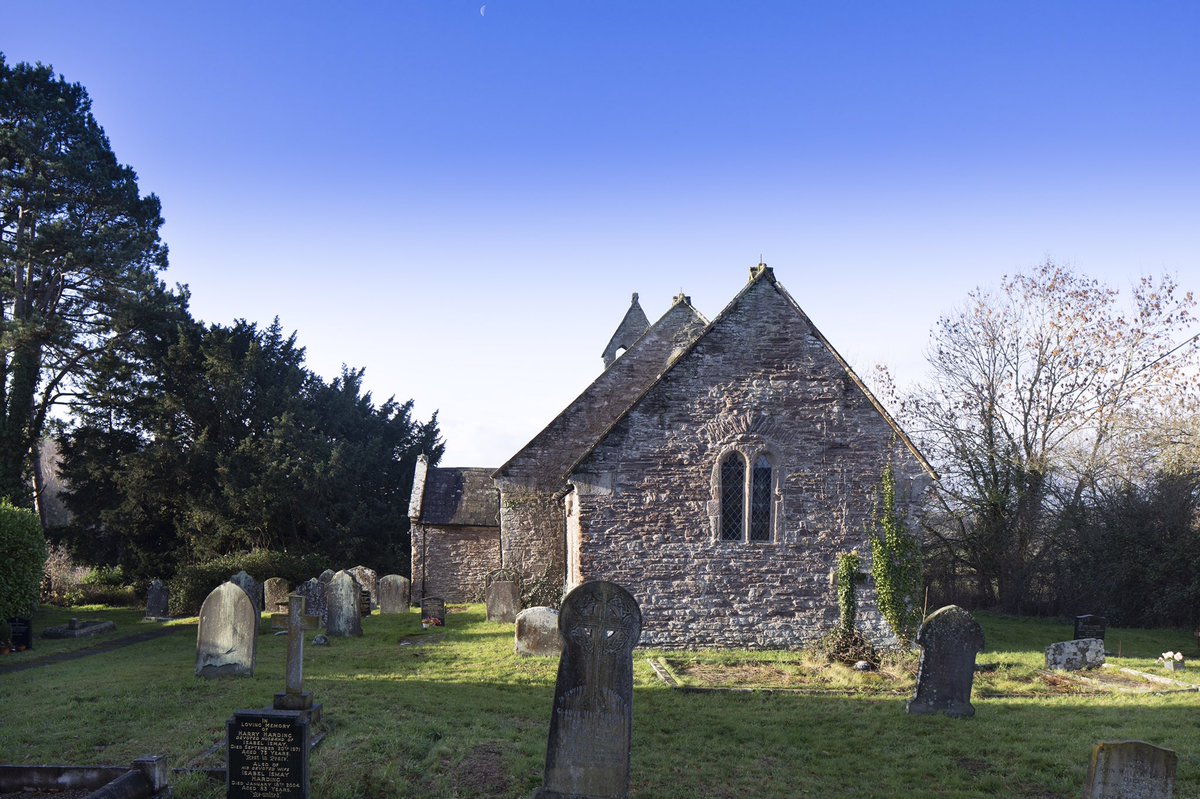 An old stone church in a graveyard. There is a window with round tops, and ivy on the wall.