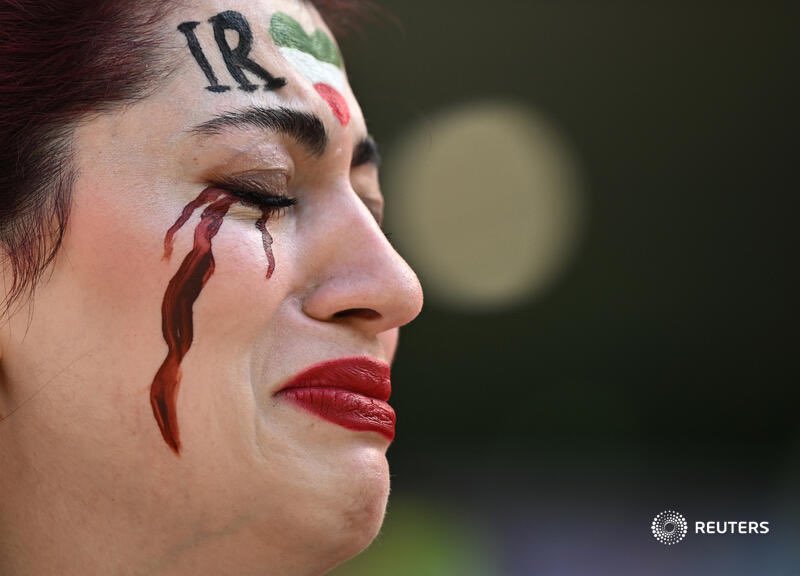historiente's tweet photo. Siguen las manifestaciones en #Qatar2022 Esta vez durante el partido de hoy entre #Irán y #Galés. Una mujer con lágrimas pintadas de color rojo oscuro sostenía una camiseta de fútbol con "Mahsa Amini #22".  #MashaAmini #Iran #IranRevolution #WomenLifeFreedom https://t.co/hD8cvETA6K