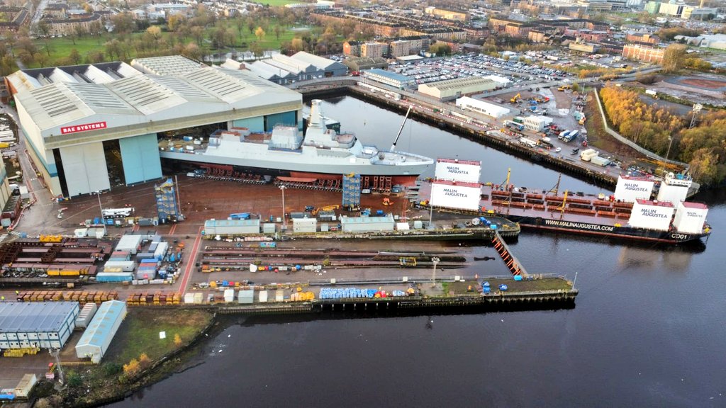 UKDefJournal's tweet photo. Drone imagery shows new warship HMS Glasgow, first of eight new Type 26 Frigates being built in Scotland, being moved onto a barge ahead of the vessel entering the water for the first time over the next week. https://t.co/NbSkuHepnP