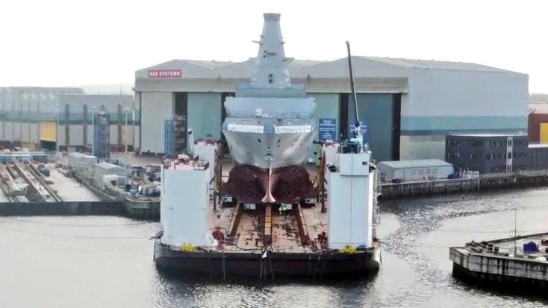 UKDefJournal's tweet photo. Drone imagery shows new warship HMS Glasgow, first of eight new Type 26 Frigates being built in Scotland, being moved onto a barge ahead of the vessel entering the water for the first time over the next week. https://t.co/NbSkuHepnP