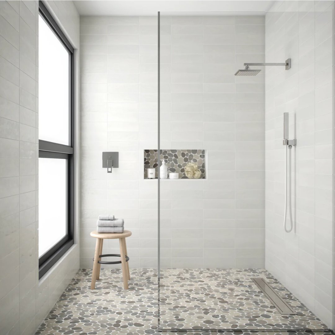Level Pebble from Island Stone in the shower is a dramatic way to bring serenity to your project. Paired with our Nomad Ceramic tile in Utopia Gloss gives this bathroom a uniquely modern serene feel. #pebbletile #islandstone #islandstonetile #tileadventure #floortile #tileinspo