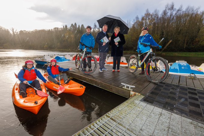 Minister Heather Humphreys standing on a dock on the edge of a lake alongside two mountain bikers and two kayakers.